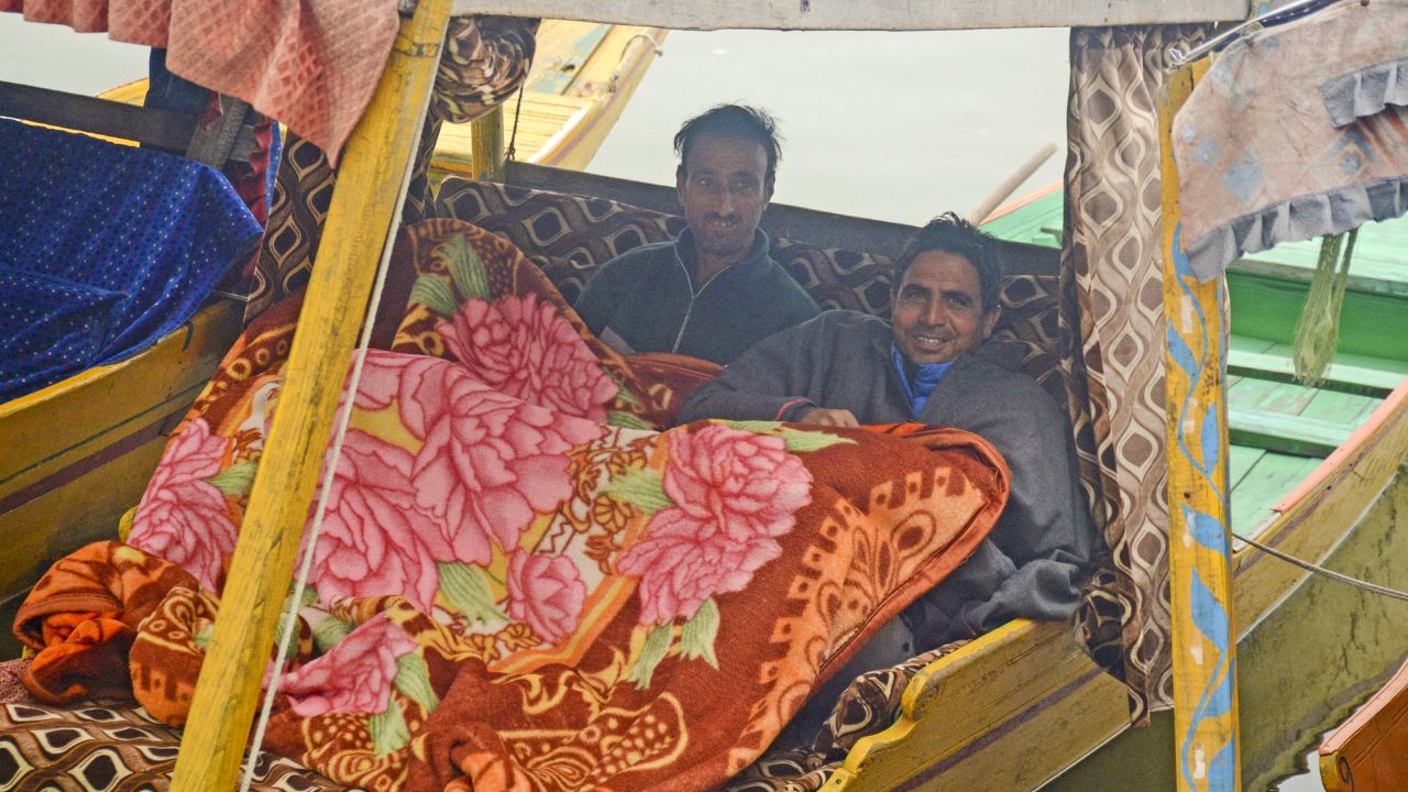 People move quietly, wrapped in warm Pashmina shawls and Kashmiri pherans, their faces hidden behind scarves or masks. (In Pic: Shikara owners warm themselves with a blanket at the Dal Lake on a foggy winter afternoon, in Srinagar on Saturday)